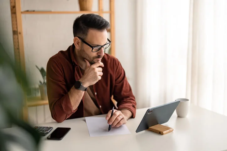 Male business person using digital tablet e-learning or remote working at home office, looking at digital tablet watching webinar, learning training, studying online seminar or video calling for work meeting.