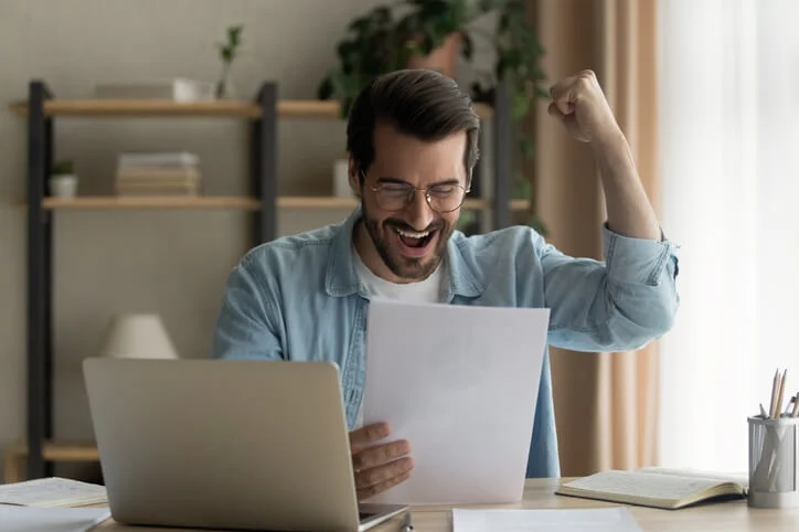 Hacking out accomplishment. Motivated male student sit by desk read official letter about admission to college university of dream. Excited young manager hold paper document confirming important deal